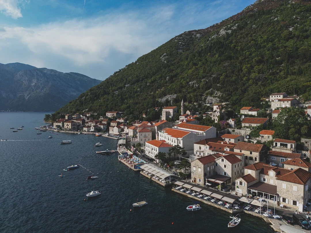 Aerial: Bay of Kotor, Montenegro. Yachts dot the blue water, framed by medieval towns & towering mountains.